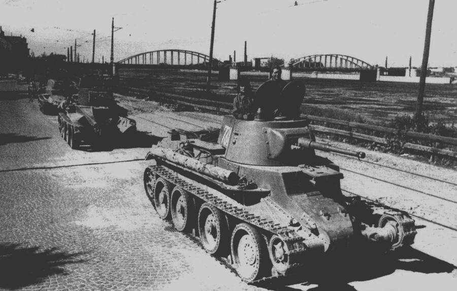 Советские танки БТ-7 (впереди колонны) и БТ-5 (за ним) двигаются на фронт на фоне Володарского моста через Неву в Ленинграде, 1943 год