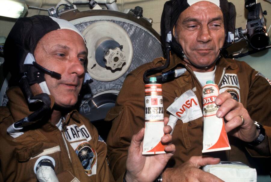Астронавты Томас Стаффорд (слева) и Дональд Слейтон держат в руках шуточный подарок Алексея Леонова — тюбики с «водкой», в которых оказался борщ из набора питания советских космонавтов