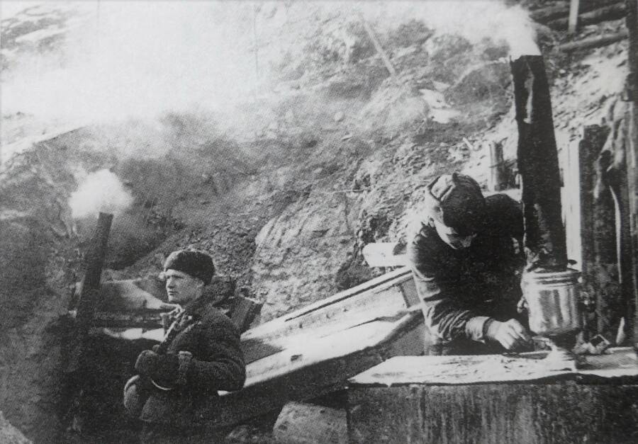 Красноармейцы у входа в блиндаж в Сталинграде. У солдата, стоящего слева, на голове ушанка, у разводящего самовар справа — зимний суконный шлем-буденовка