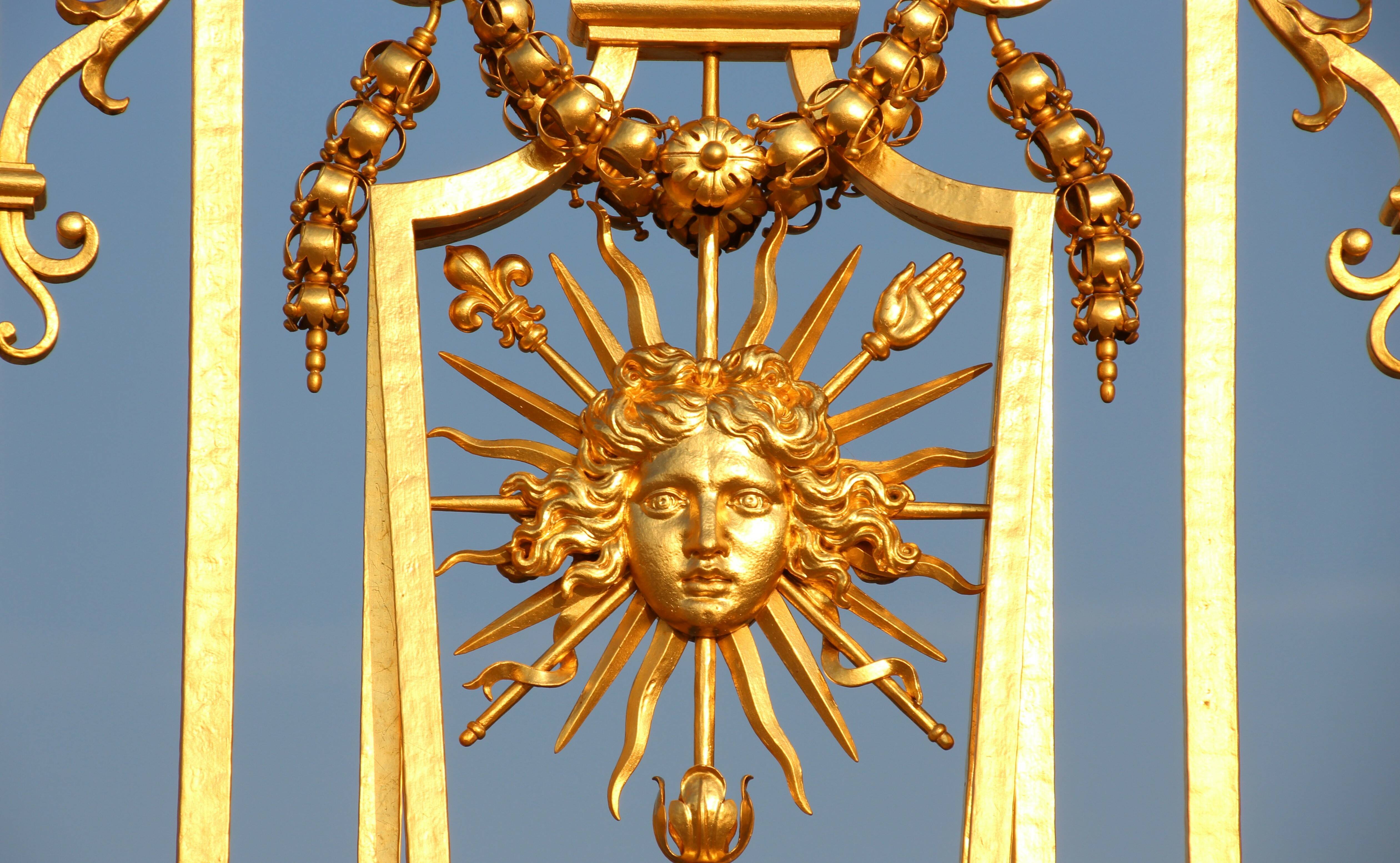 Эмблема короля-солнца с головой Аполлона, лучами и скипетром с французской лилией. Фрагмент ворот в Версале (фото: Lionel Allorge CC BY-SA 3.0)