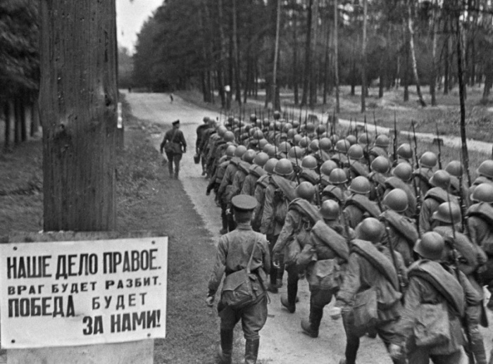 Плакат с лозунгом «Наше дело правое» на обочине подмосковной лесной дороги, по которой марширует колонна советских пехотинцев, 23 июня 1941 года